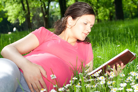pregnant woman reading outside in the grass