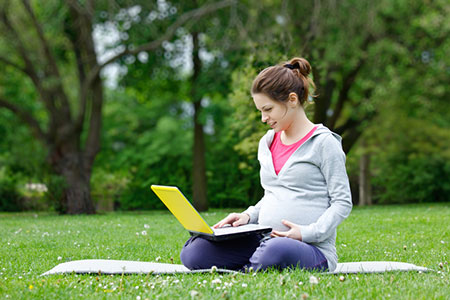 pregnant woman sitting outside with her laptop